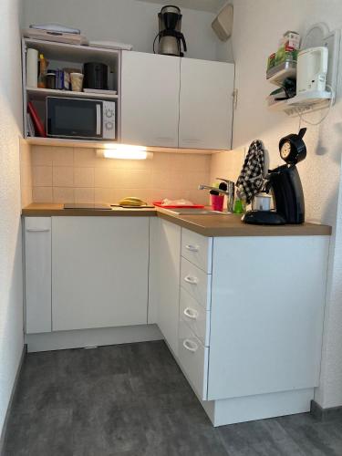 une petite cuisine avec des armoires blanches et un micro-ondes dans l'établissement La Pinède de Saint Georges, à Saint-Georges-de-Didonne