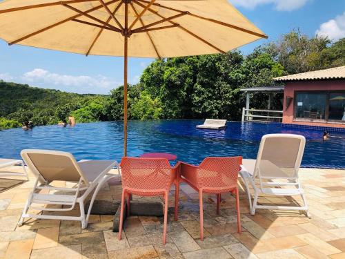 uma mesa com cadeiras e um guarda-sol ao lado de uma piscina em Villas do Pratagy Maceió em Maceió