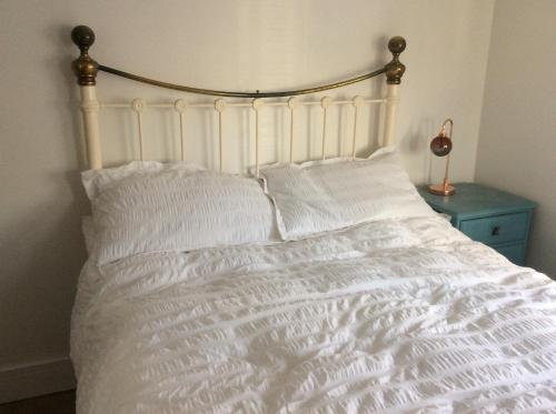 a white bed with white pillows and a blue table at Tremeer Cottage in Upper Beeding