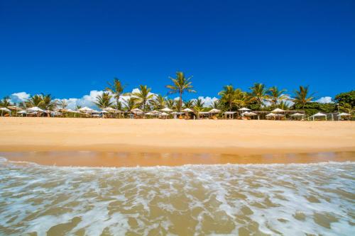 a beach with umbrellas and palm trees and the ocean at Travel Inn Pousadas & Beach Club Trancoso in Trancoso