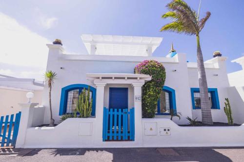 ein weißes Haus mit blauen Türen und einer Palme in der Unterkunft Villa Tiguaro Piscina Climat Jacuzzy AC Villa 9 12 in Corralejo