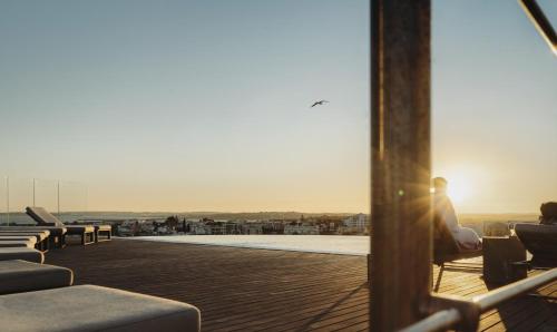 a person sitting on a roof watching the sunset at Longevity Health & Wellness Hotel - Adults Only in Alvor