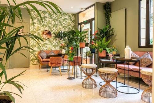una sala de estar con mesas, sillas y plantas. en Hotel Ariane Montparnasse by Patrick Hayat, en París