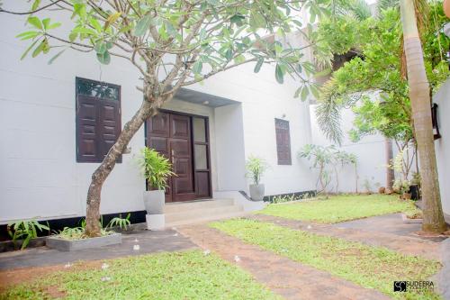 a white house with a tree in front of it at Blooming polhena in Matara