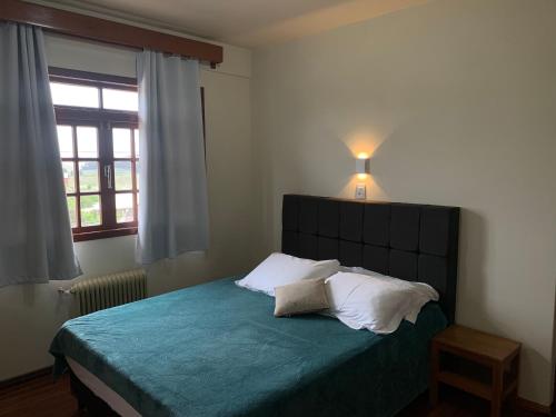 1 dormitorio con 1 cama con manta azul y ventana en Altos da Serra Hotel, en São Joaquim