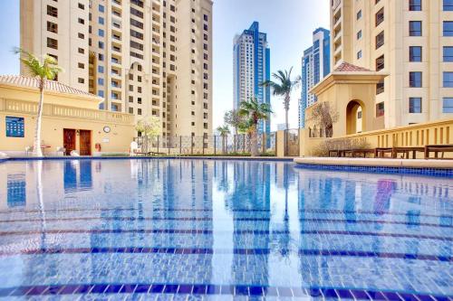 a large swimming pool in a city with tall buildings at Modern, Luxe & Spacious 4-Bed Condo, Full Kitchen, 3 Min walk to Beach, Tram & Marina By "La Buena Vida Holiday Homes" in Dubai