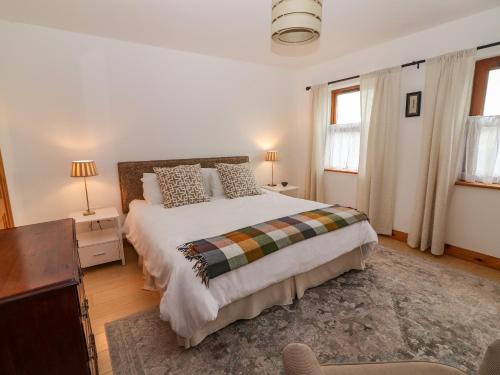 a bedroom with a large bed and two windows at Cherry Blossom Cottage in Ennis