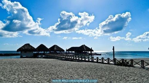 a pier with huts on a beach with the ocean at Elegante Blue Marine Apartamento Juan Dolio in Juan Dolio