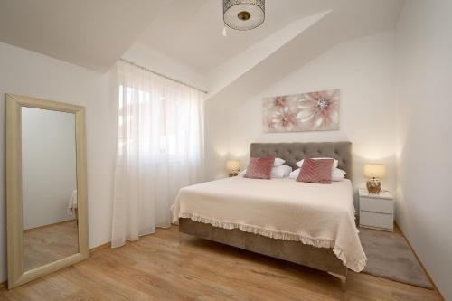 a white bedroom with a large bed and a mirror at Zora Residence in Kaštela