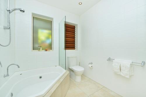 a white bathroom with a tub and a toilet at Villa Frangipani in Port Douglas