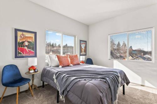 a bedroom with a bed and a blue chair and two windows at New 2 Bed 2 Bath Near Perry District and DT in Spokane