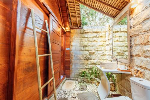 a bathroom with a toilet and a stone wall at Bila Penida Resort & Farm in Nusa Penida