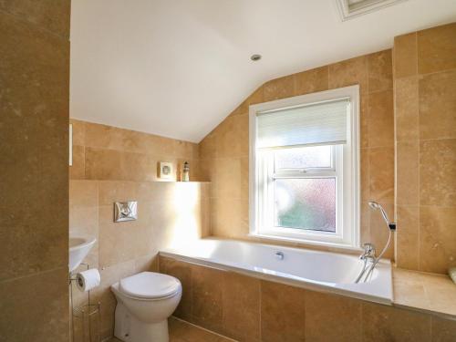 baño con bañera, aseo y ventana en South Harbour Cottage en Weymouth
