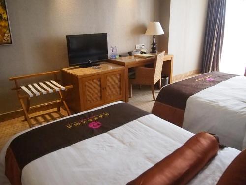 a hotel room with two beds and a desk with a television at Wenchang Waika Hotel in Wenchang