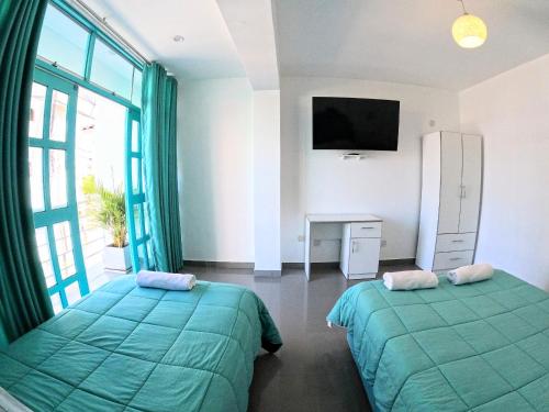 a bedroom with two beds and a tv and a window at AQUAMARINE PARACAS Beach Hostal in Paracas