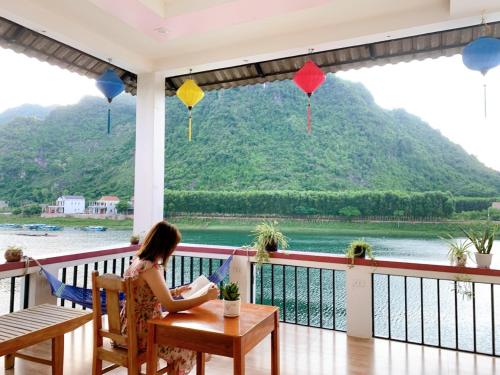 a woman sitting at a table on a balcony looking out at the water at Funny Monkeys Homestay in Phong Nha