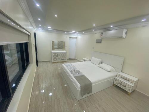 a white bedroom with a bed and a chair at Dar Al Hamra Rest إستراحة دار الحمراء in Al Ḩamrāʼ