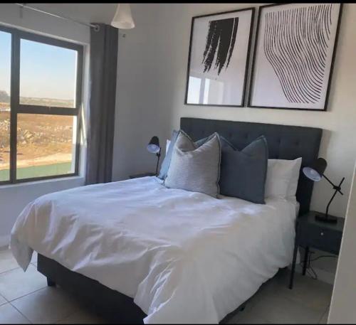 a bedroom with a large white bed with two windows at Taina Apartment @ Green Creek in Pretoria