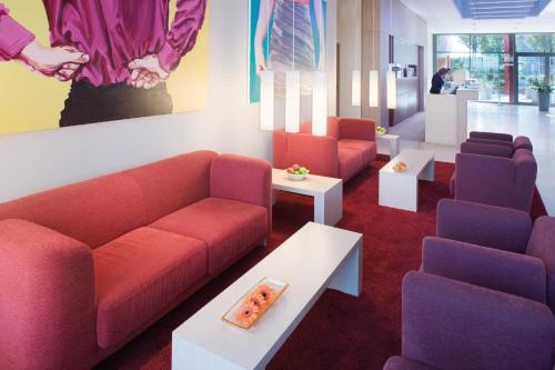 a waiting room with couches and tables and a painting at Mövenpick Hotel Frankfurt City Messe in Frankfurt/Main