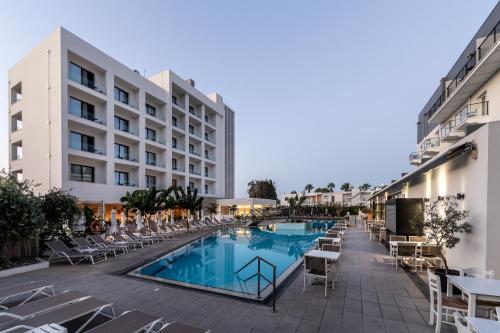 a hotel with a swimming pool and chairs and a building at Anemi Hotel & Suites in Paphos