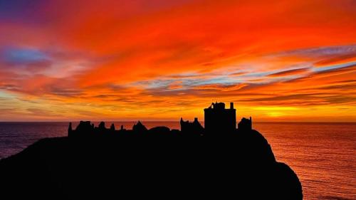 a silhouette of a castle on the ocean with a sunset at Rowanlea Caravan in Stonehaven