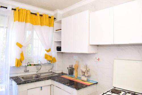 una cocina con armarios blancos y cortinas amarillas en Rorot 2 bdrm stay located Annex home away(bright), en Eldoret