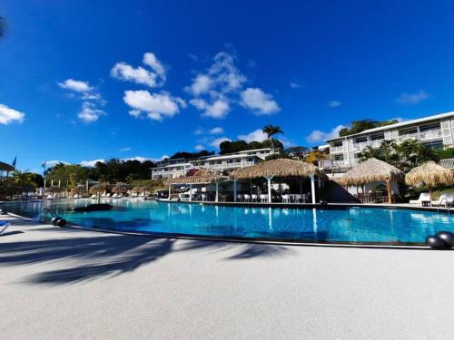 a large swimming pool with straw umbrellas on a beach at Caraïbe Diamond Studio in Le Diamant