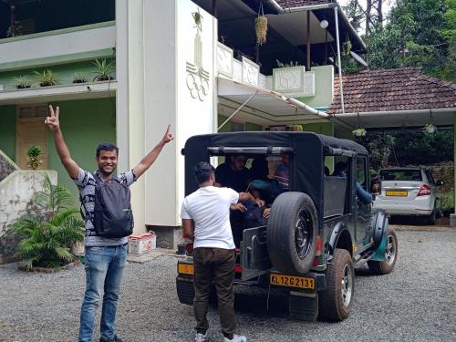 two men standing in front of a car with their arms up at Maliyeckal Homestay in Munnar