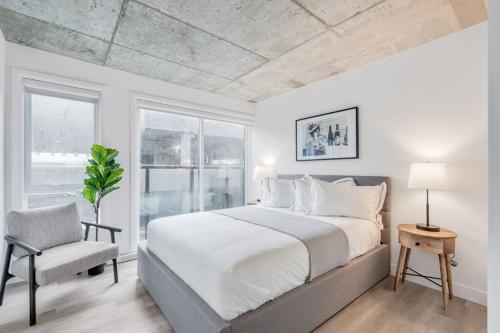 a white bedroom with a bed and a chair at Initial / Cinéma +Parking / Centre-ville de Québec in Quebec City