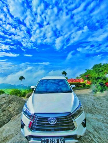 a white car parked on a gravel road with a cloudy sky at Rental Mobil Makassar in Makassar