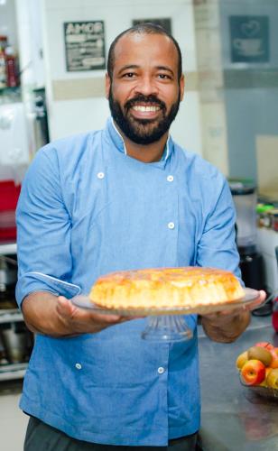a man in a kitchen holding a pizza on a plate at Pousada e Hostel Chez Marianne in Salvador
