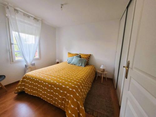 1 dormitorio con 1 cama con edredón amarillo y ventana en Casteljaloux Appartement 2 chambres balcon parking résidence calme, en Casteljaloux