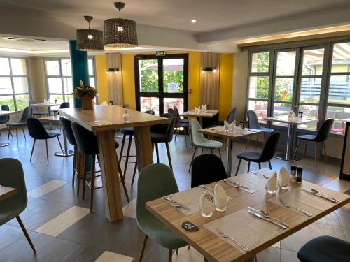 een restaurant met houten tafels, stoelen en ramen bij Campanile Saumur in Saumur