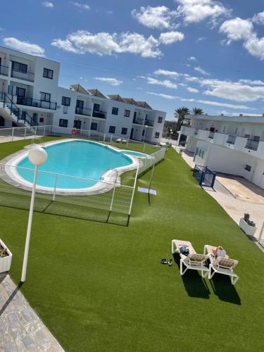 an outdoor swimming pool with green grass and two chairs at Costa Calma Sun & Beach Apartment - wifi & pool in Costa Calma