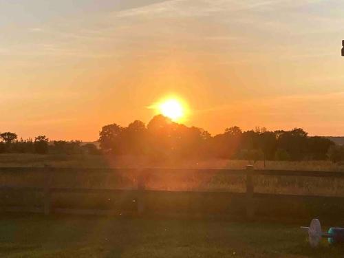 a sunset over a field with a fence and trees at Farmhouse Resort in Midhurst