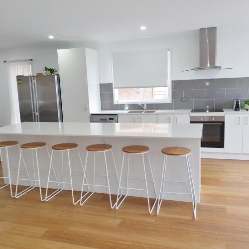 a kitchen with a white counter and stools at Tuggerah lakefront 4 bed 2 bath home with stunning views in Gorokan