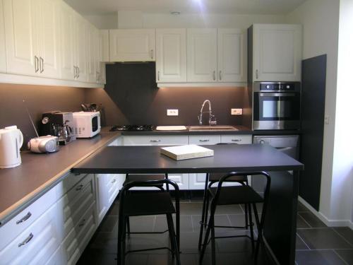 une cuisine avec des armoires blanches et une table avec des tabourets dans l'établissement Maison rénovée près de la Forêt de Tronçais, grand jardin, cheminée, wifi, animaux acceptés - FR-1-489-128, à Urçay