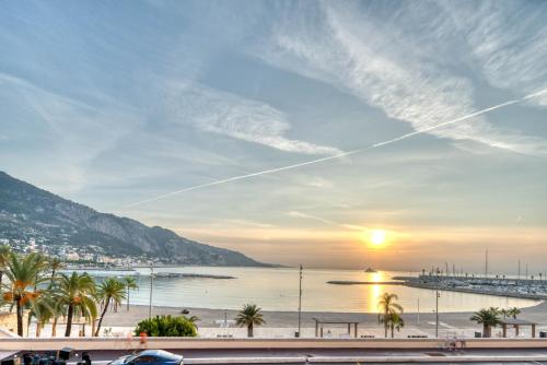 a sunset over a beach with palm trees and the ocean at Apartment les Sablettes panoramic sea view in Menton