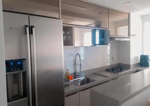 cocina con armarios blancos y nevera de acero inoxidable en Apartamento luxuoso com infra completa próximo a Praia da Barra da Tijuca, en Río de Janeiro