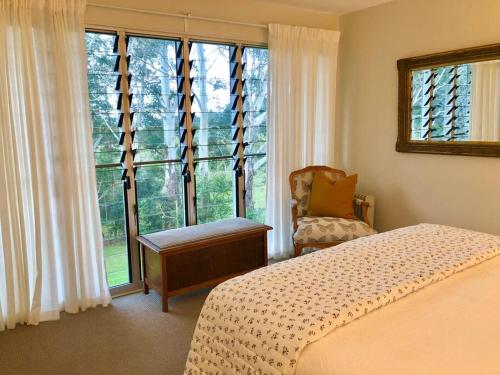 a bedroom with a bed and a chair and a window at "La Petite Grange" Maleny in Maleny