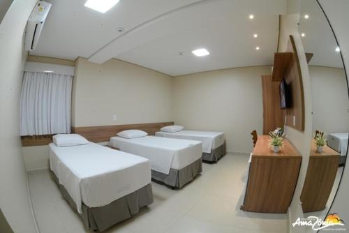 a hospital room with three beds and a television at Hotel Portal da Amazônia in Várzea Grande