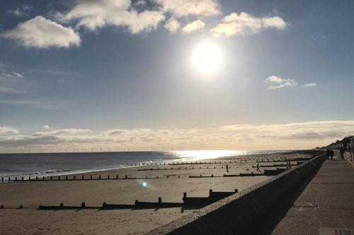 a beach with benches and the sun in the sky at Edwardian Villa by the Sea Coastal Walks King Beds in Walton-on-the-Naze