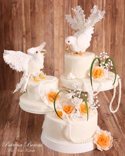 a three tiered wedding cake with white birds and orange roses at Hotel Schäfflerhof in Bischofsmais