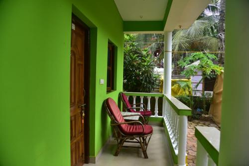a porch with two chairs and a green wall at Jardim a Mar in Agonda
