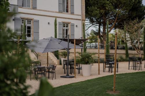 a patio with tables and chairs and an umbrella at Hôtel-Restaurant Villa Métis in Les Herbiers
