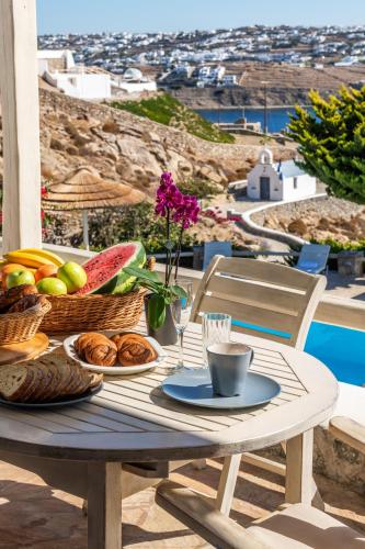 a table with a breakfast of fruit and bread on a balcony at Yalos Mykonos Ornos Pouli private apartments w shared swimming pool in Mýkonos City