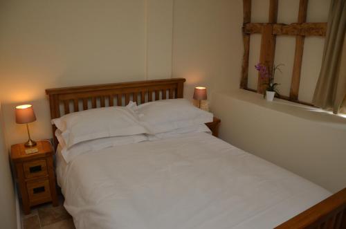 uma cama com lençóis brancos e almofadas num quarto em Sabine Barn em Oxford