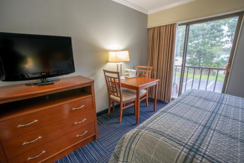 サウス・ヤーマスにあるAll Seasons Resort, Trademark Collection by Wyndhamのベッド、デスク、テレビが備わるホテルルームです。