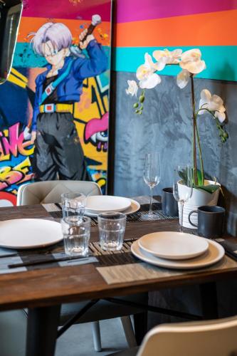 a wooden table with plates and glasses and a painting at Capsule Art Déco - Jacuzzi - Netflix - Home Cinéma - Arcade de jeux & Nintendo switch - 2 chambres - Filet suspendu in Valenciennes