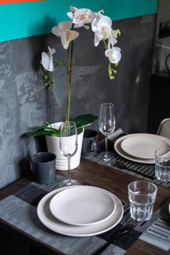 a table with plates and glasses and a vase with flowers at Capsule Art Déco - Jacuzzi - Netflix - Home Cinéma - Arcade de jeux & Nintendo switch - 2 chambres - Filet suspendu in Valenciennes